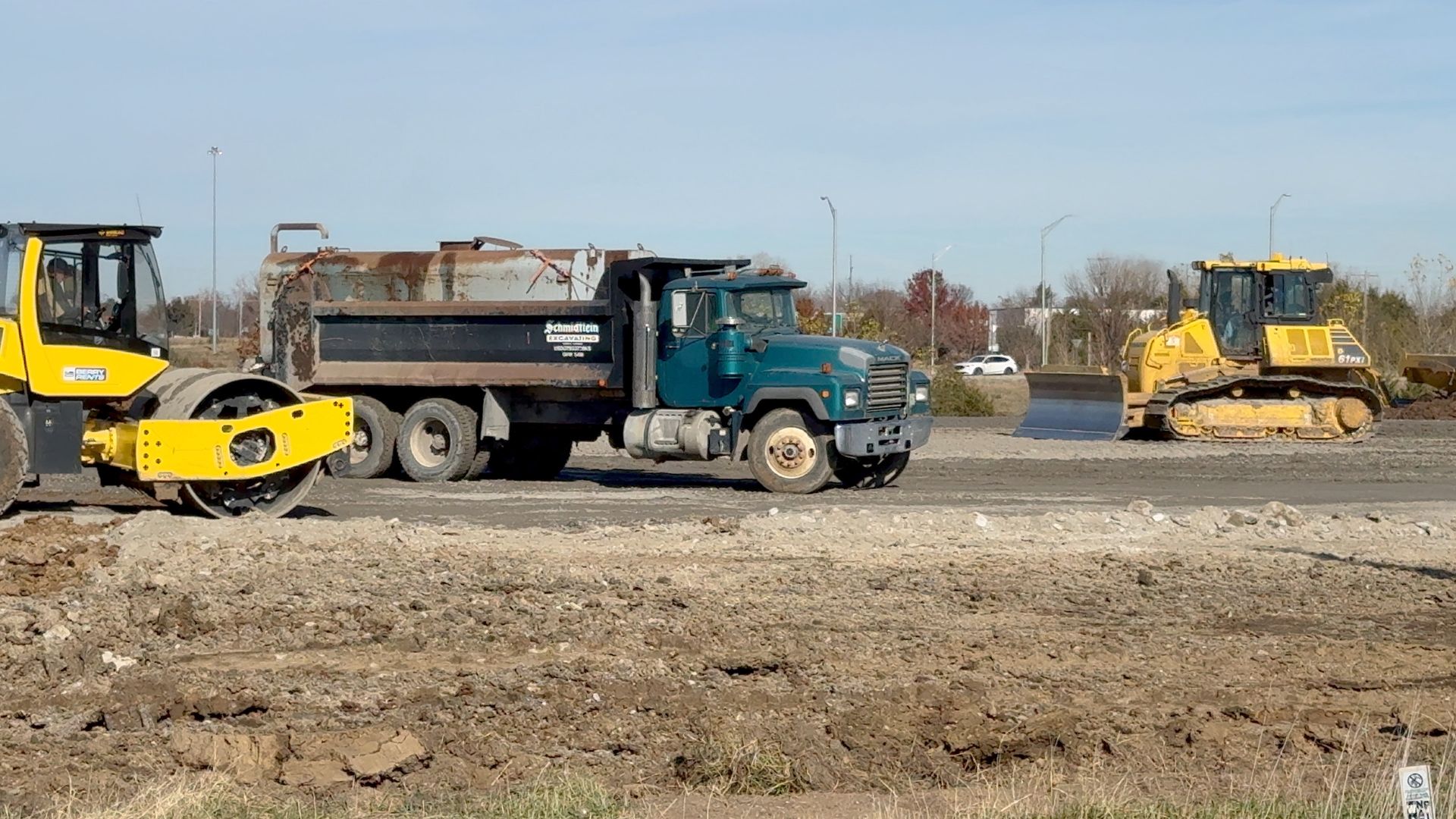 A dump truck is driving down a dirt road next to a bulldozer.