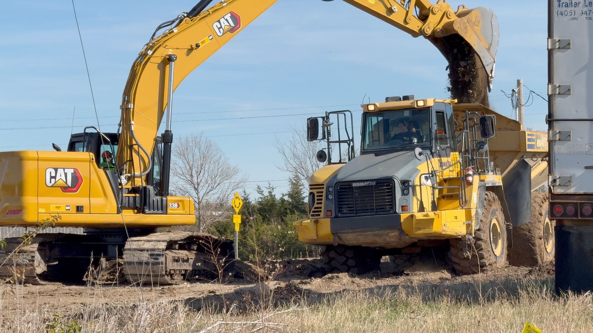 A cat excavator is loading dirt into a dump truck.