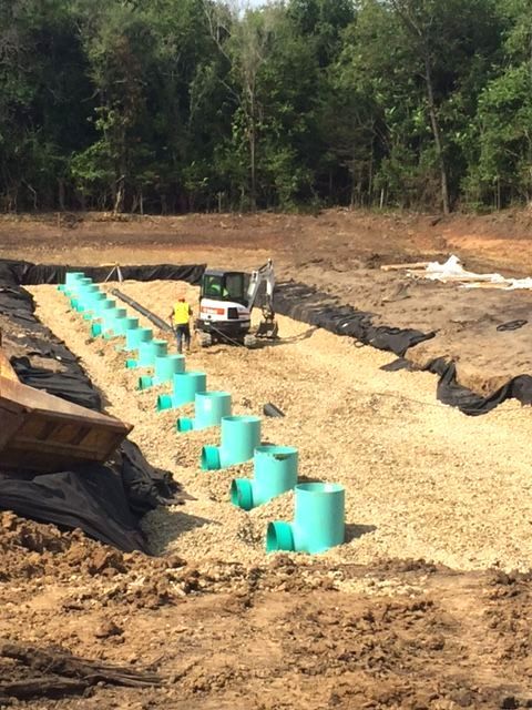 A construction site with a row of green pipes in the dirt.