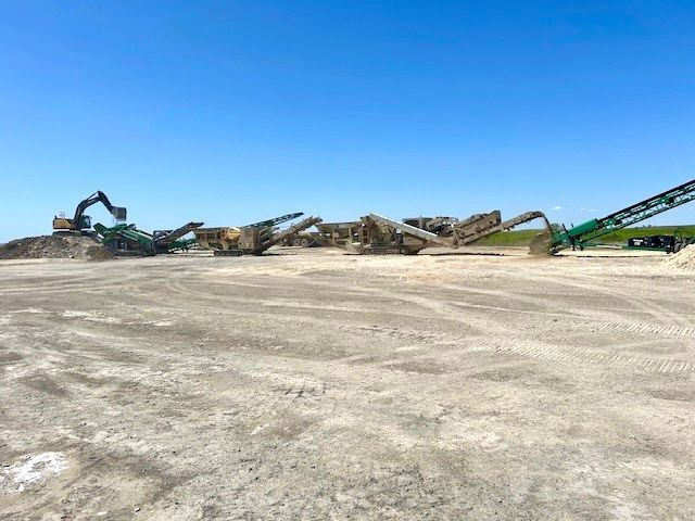 A row of construction vehicles are parked in a dirt field.