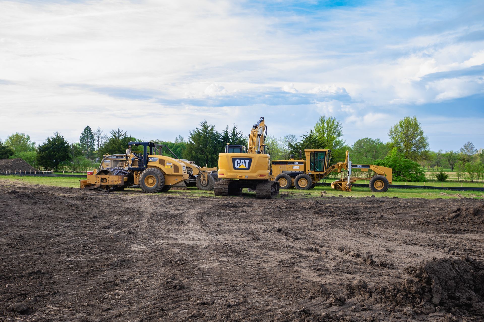 A group of construction vehicles are parked in a dirt field.