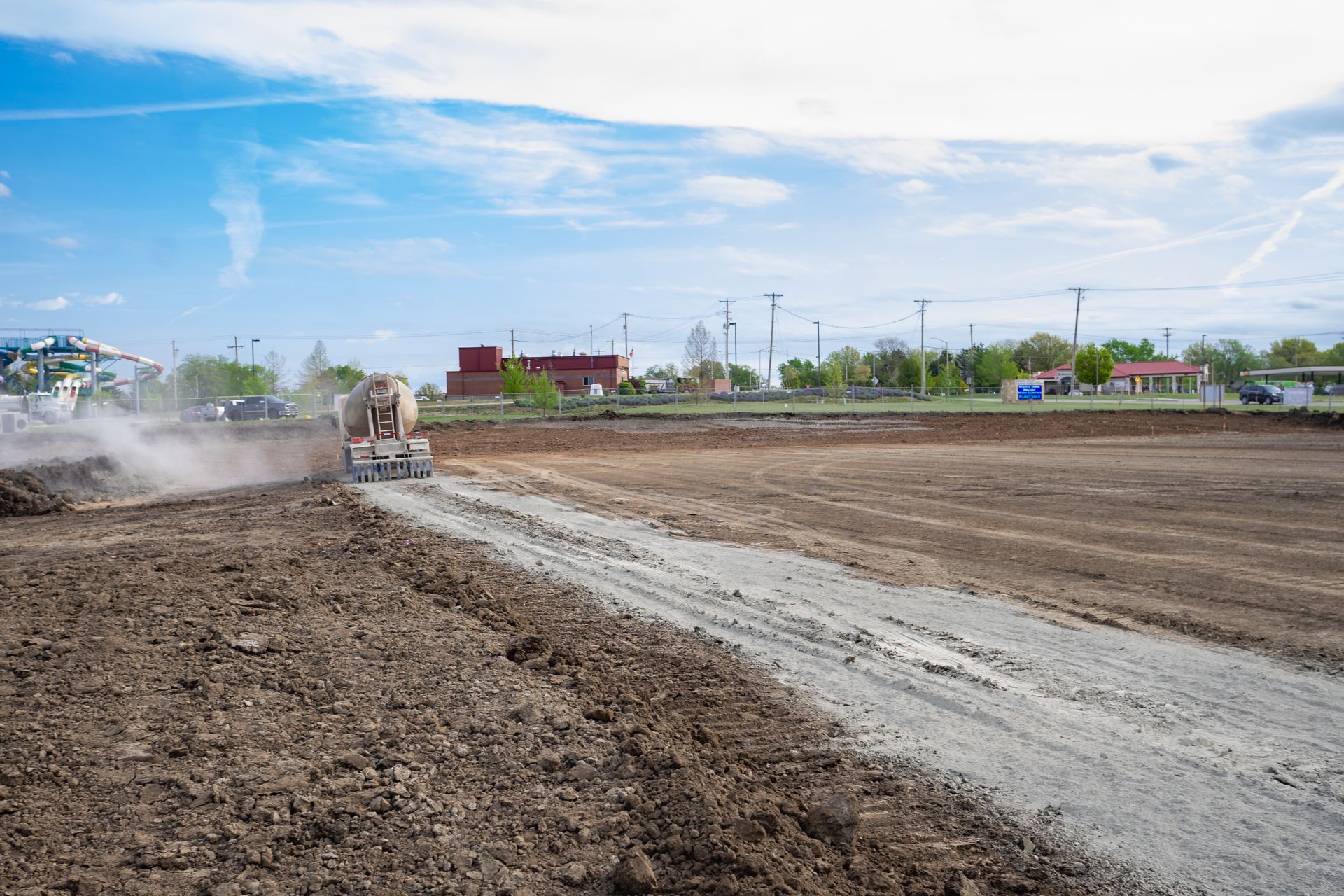 A bulldozer is spreading fertilizer on a dirt road.