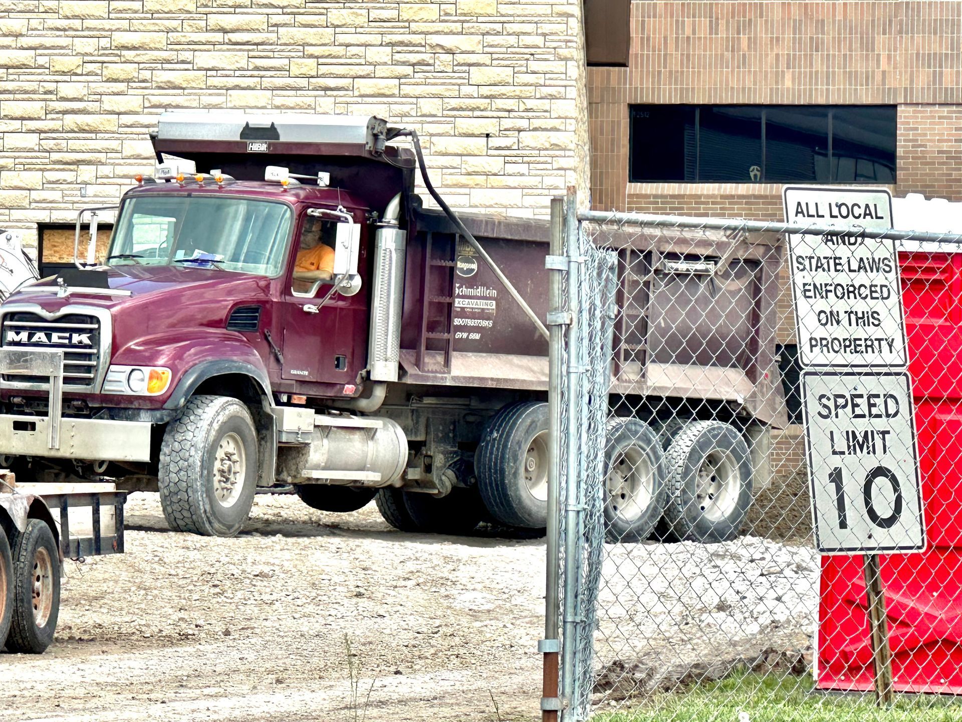 A dump truck is parked in front of a brick building behind a chain link fence.