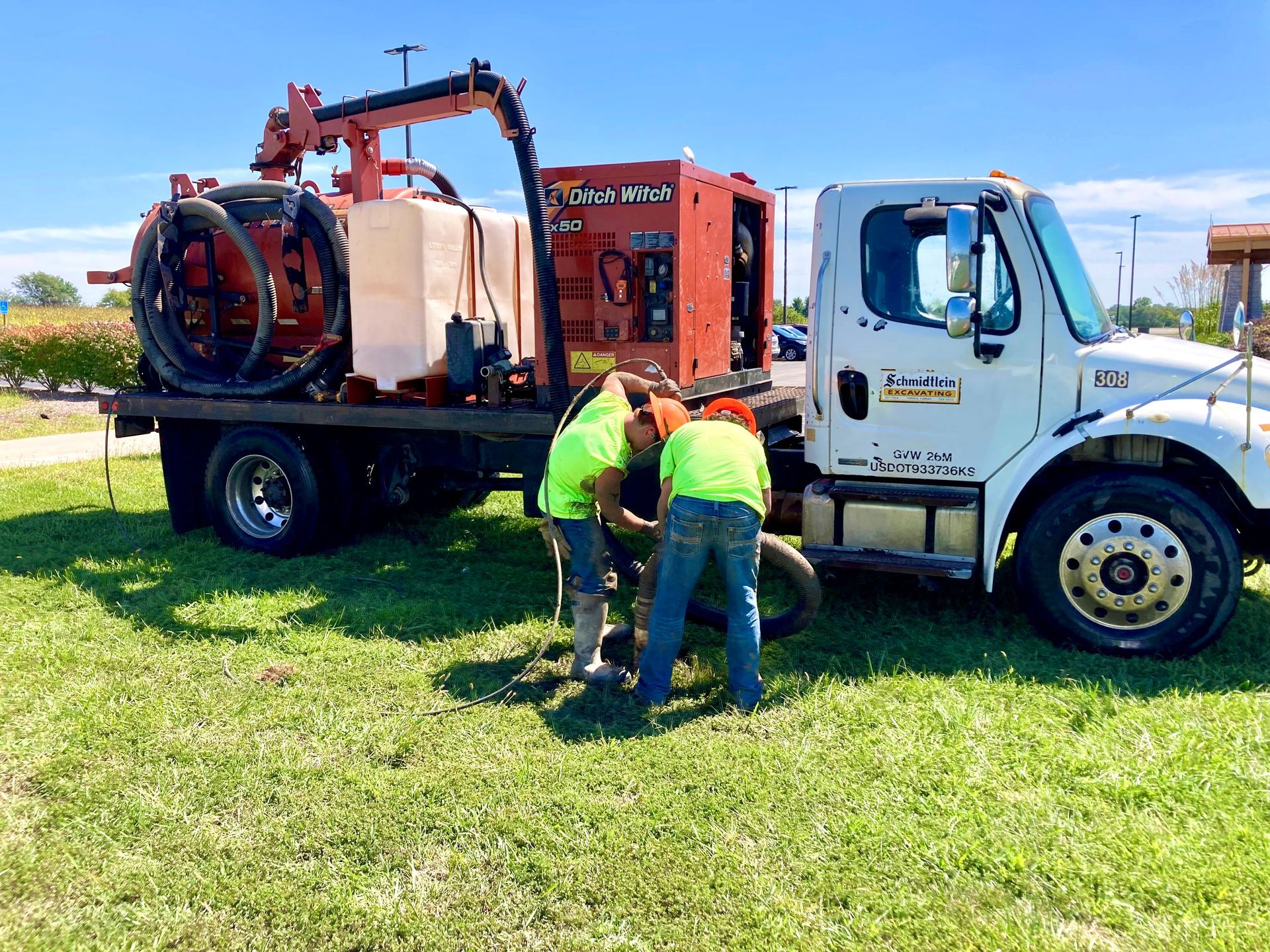 A large vacuum truck is parked on the side of the road next to a semi truck.