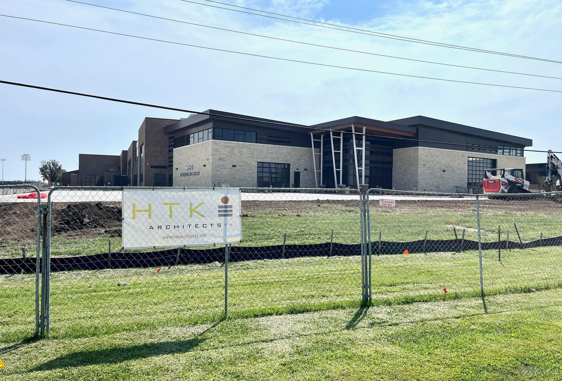 A large building under construction is behind a chain link fence.