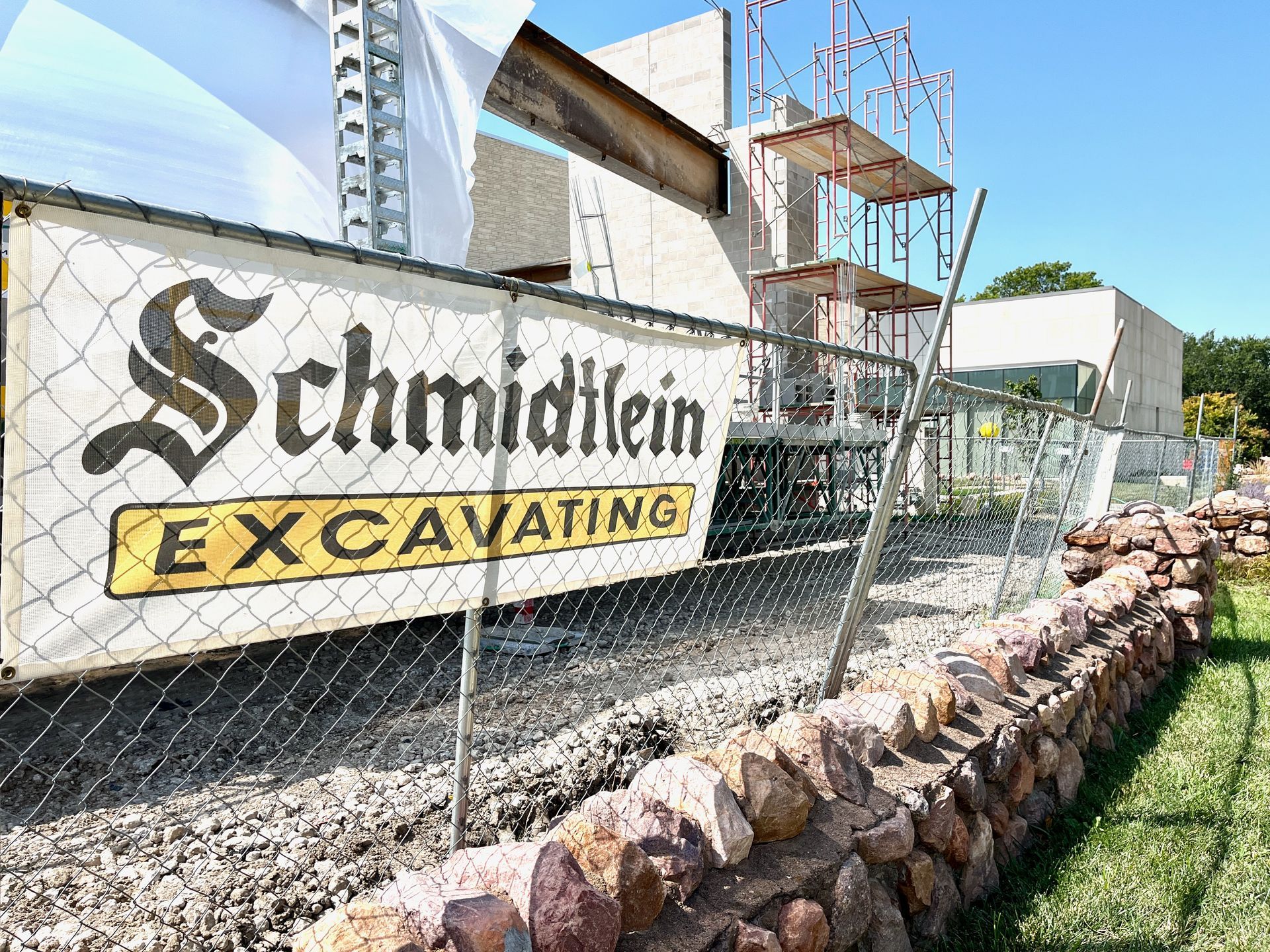 A sign for schmidtlein excavating is hanging on a chain link fence.