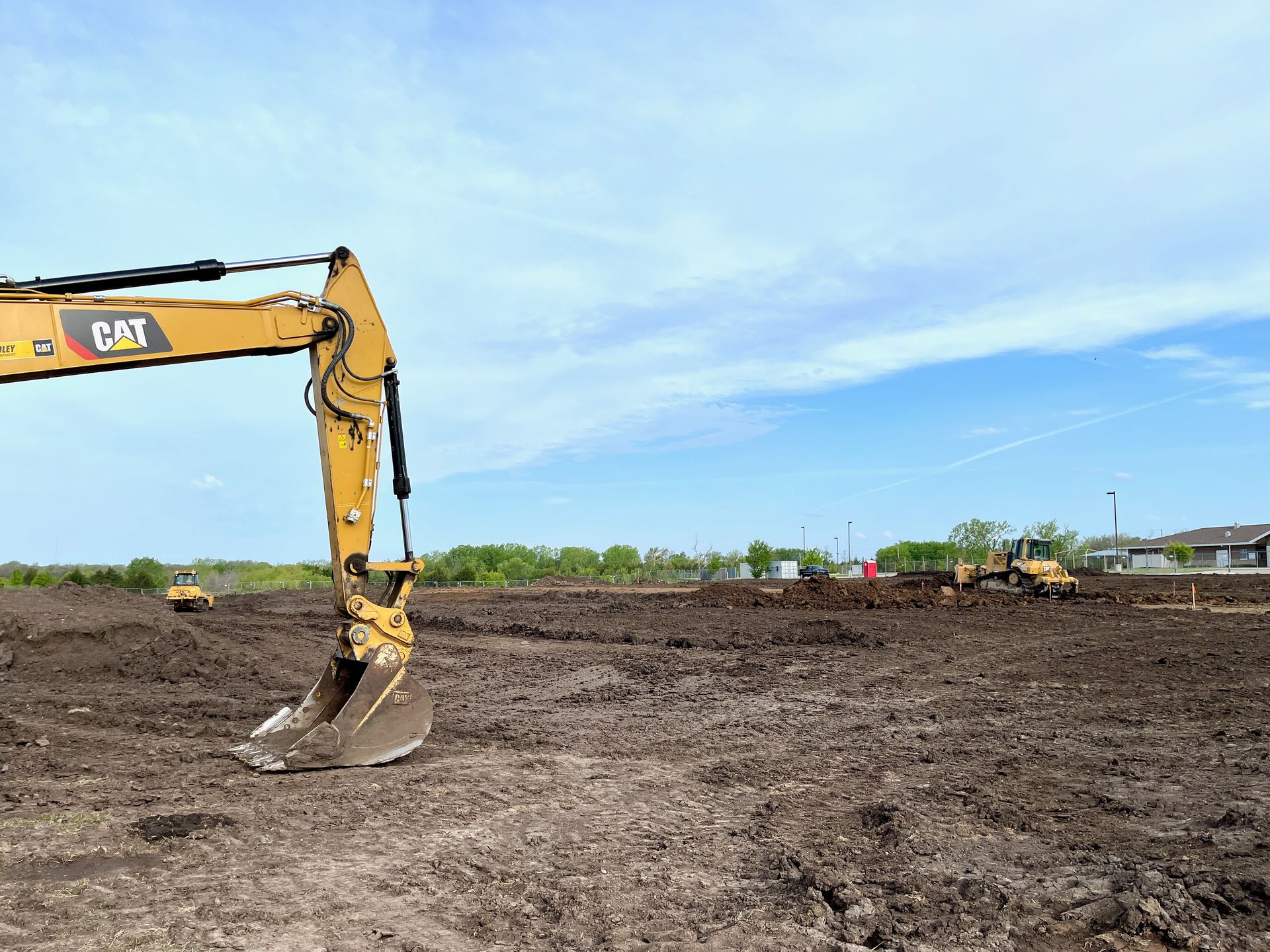 A cat excavator is sitting in the middle of a dirt field.