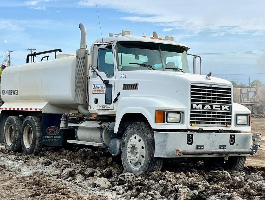 A white mack truck is driving through a muddy field.