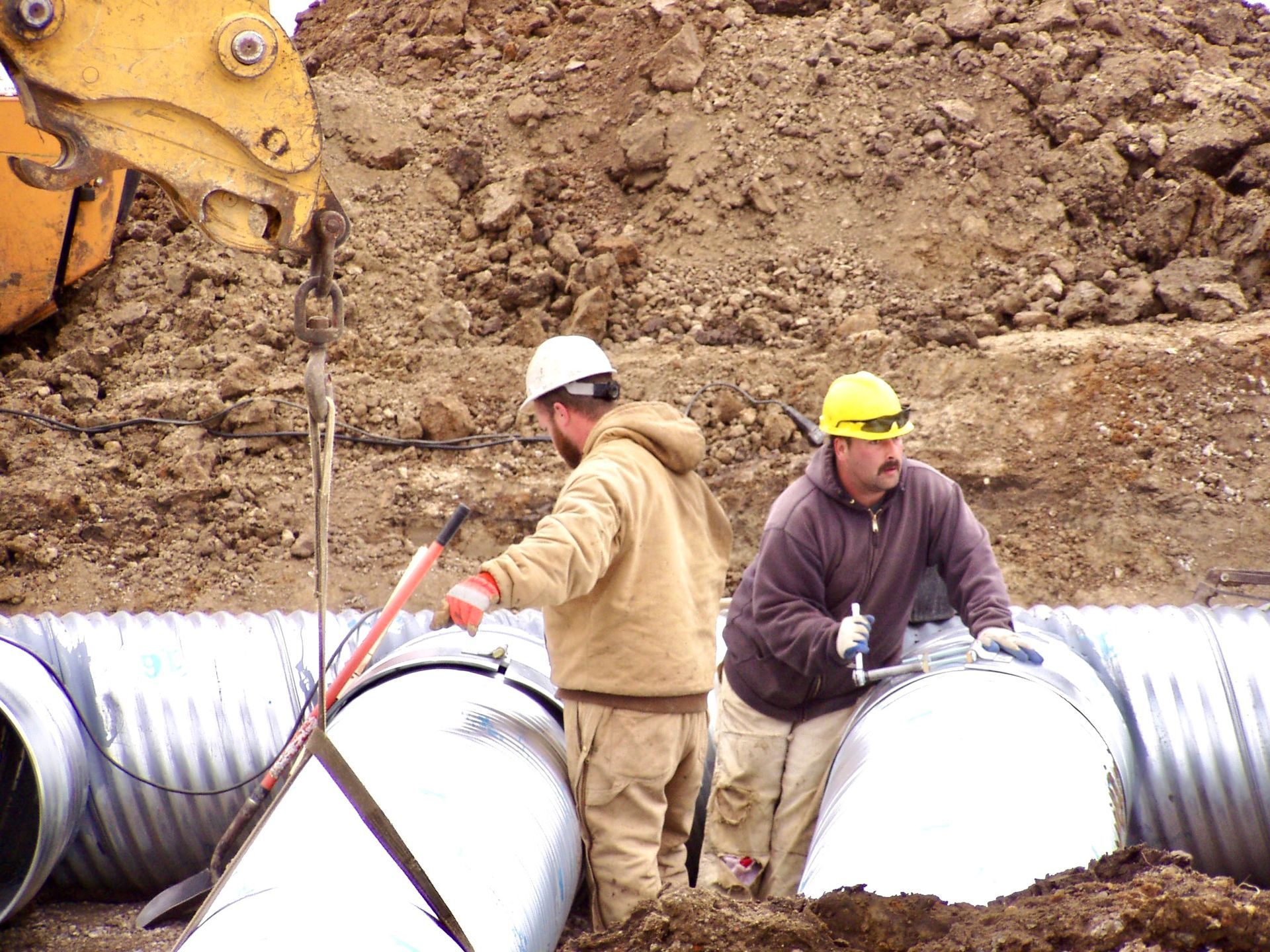 Two construction workers are working on pipes in the dirt