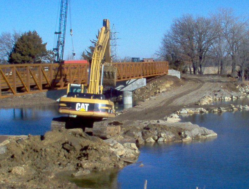 A cat excavator is working on a bridge over a body of water