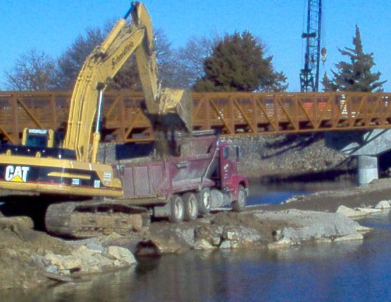 A cat excavator is working on a bridge over a body of water