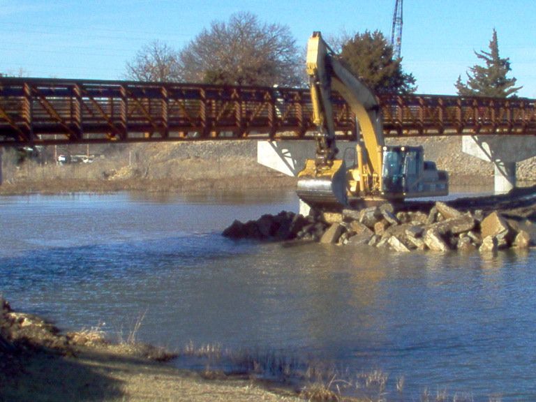 A bridge over a body of water with a yellow excavator in the foreground