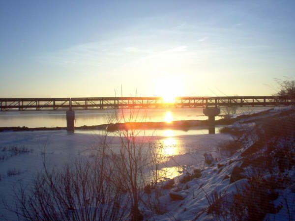 The sun is setting over a bridge over a body of water