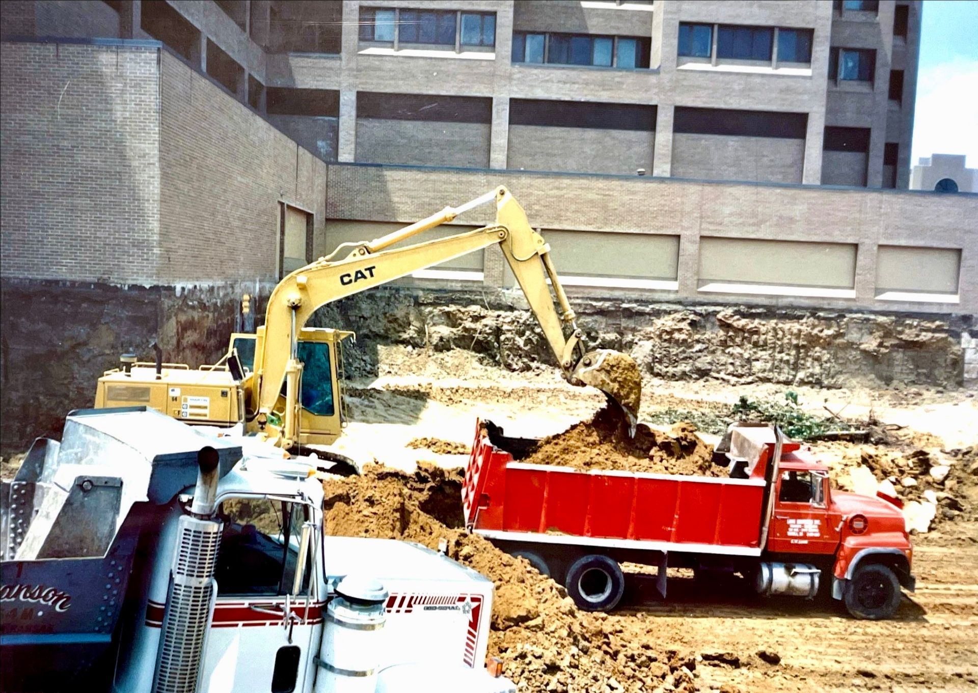 A yellow excavator is loading dirt into a red dump truck