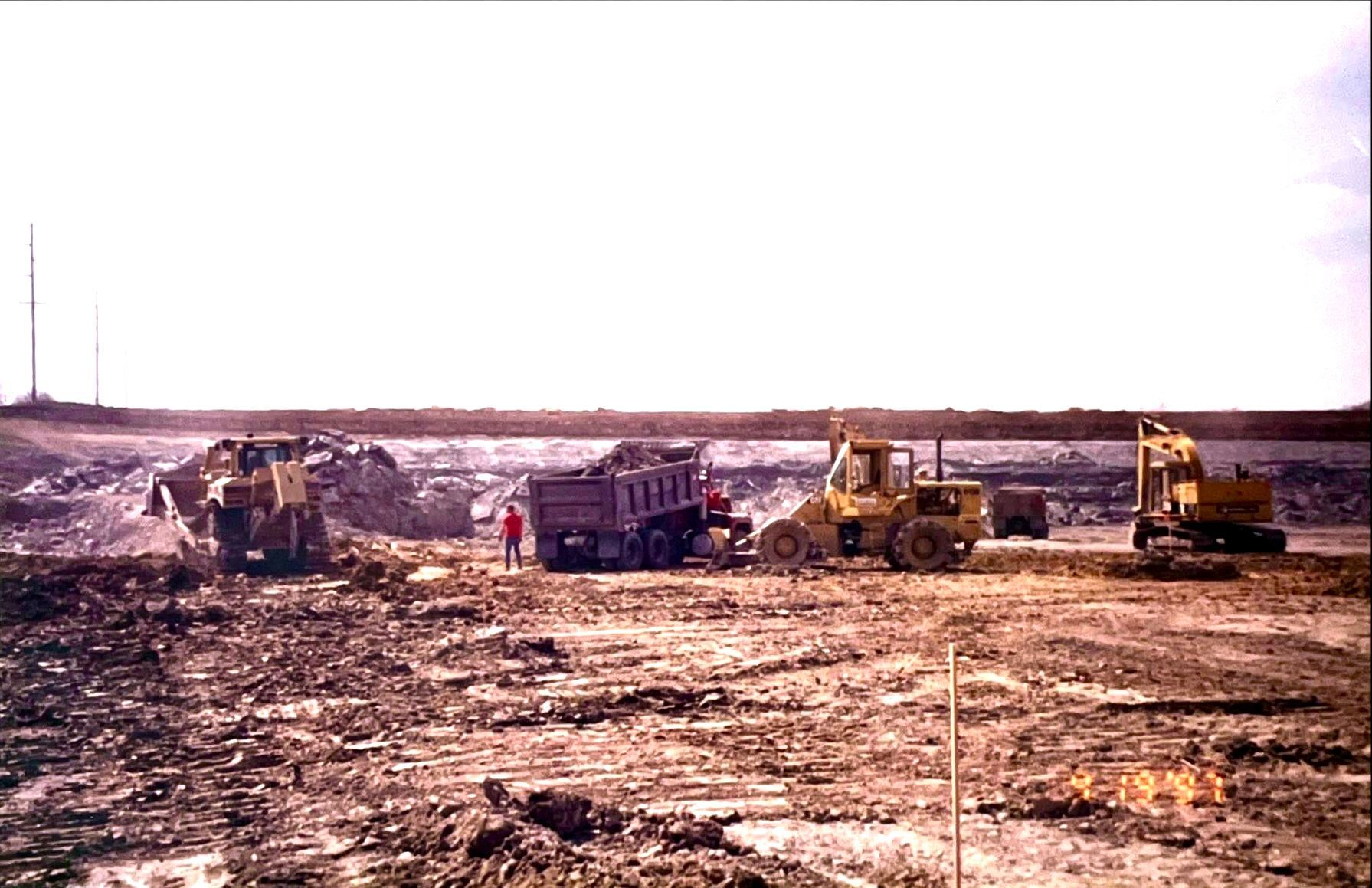 A group of construction vehicles are working on a dirt field.