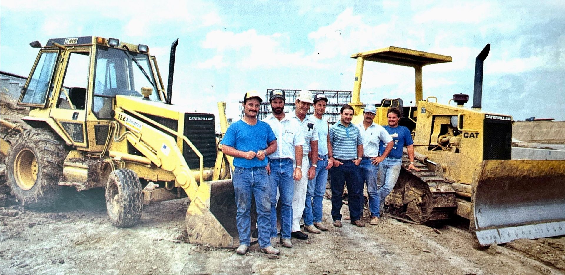 A group of men are standing in front of construction vehicles.