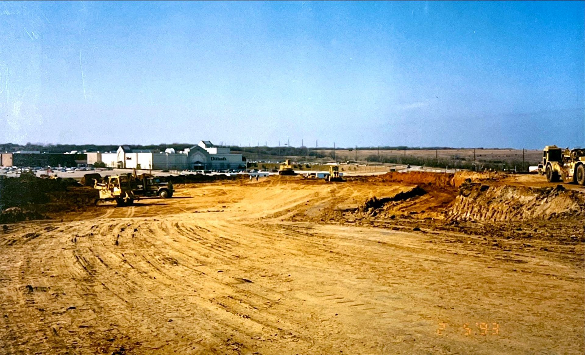 A large dirt field with a few buildings in the background