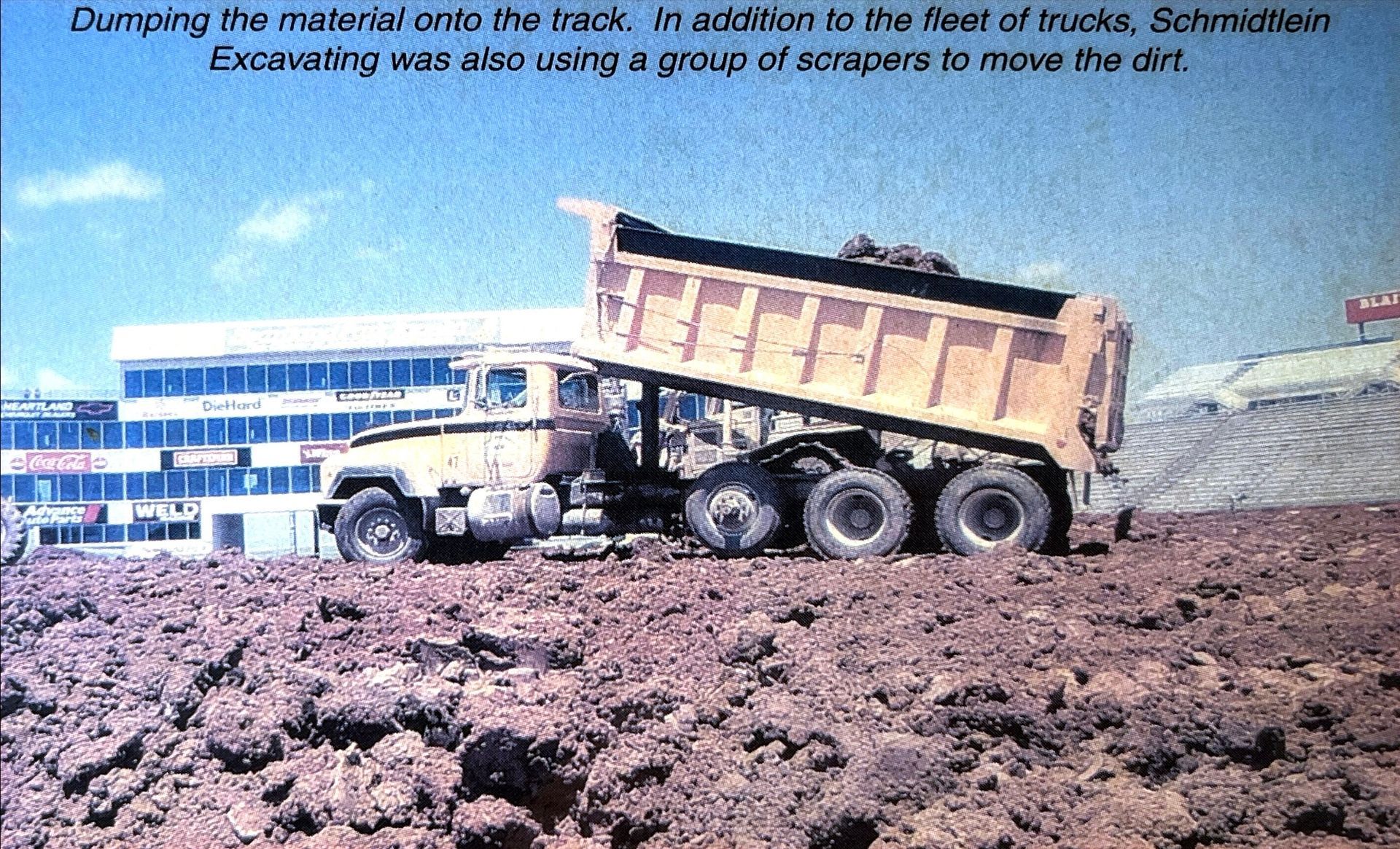 A large dump truck is driving through a dirt field