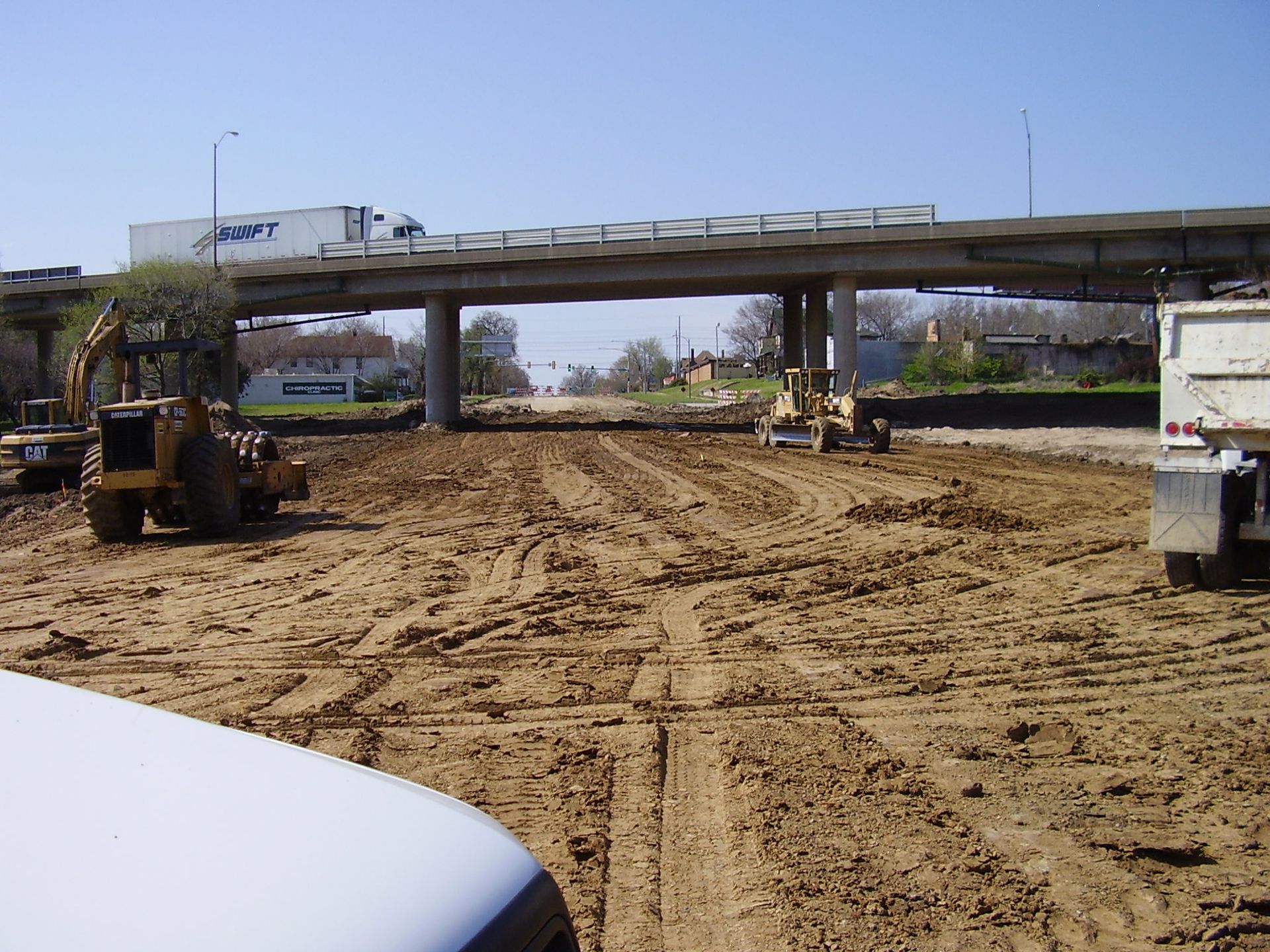 A white truck is parked in a dirt field under a bridge