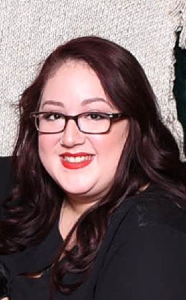 A woman wearing glasses and red lipstick is smiling for the camera.