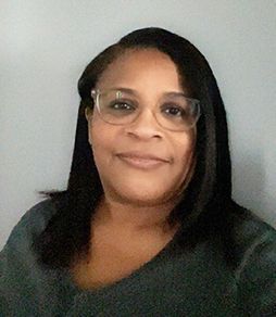 A woman wearing glasses and a gray shirt is smiling for the camera.