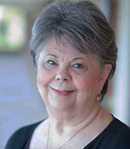 An older woman is smiling for the camera while wearing a black shirt and a necklace.