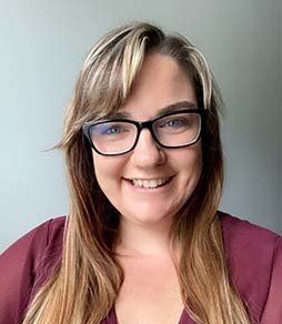A woman wearing glasses and a maroon shirt is smiling for the camera.