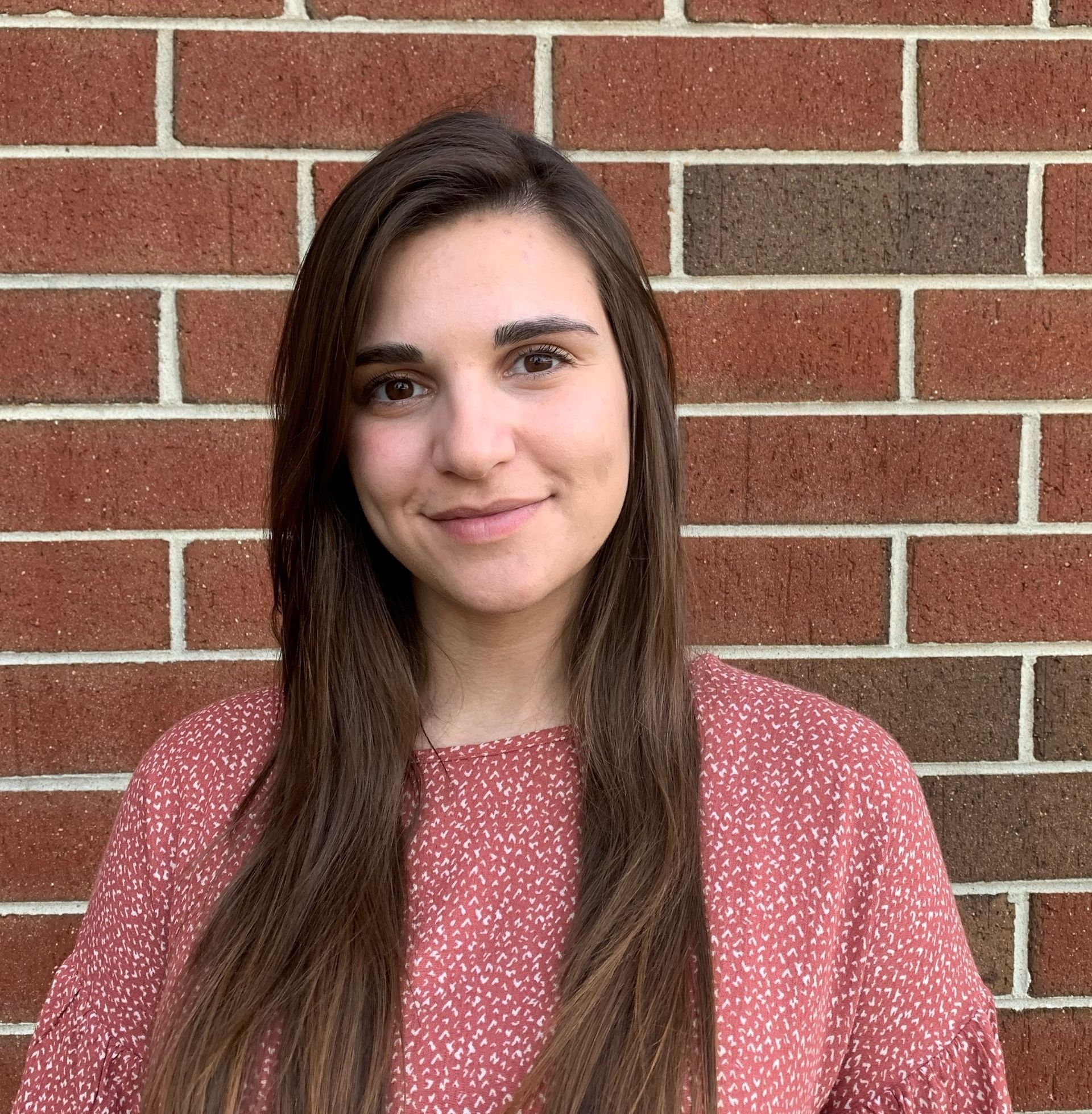 A woman in a pink shirt is standing in front of a brick wall.