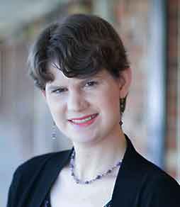 A woman wearing a black jacket and a purple necklace is smiling for the camera.