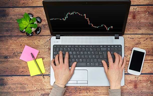 A person is typing on a laptop computer with a graph on the screen.