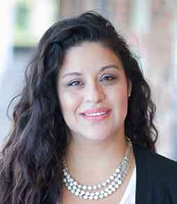 A woman wearing a pearl necklace and a black jacket is smiling for the camera.