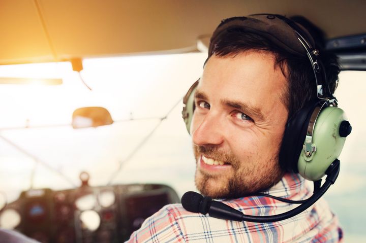 A man wearing headphones and a microphone is sitting in a plane.