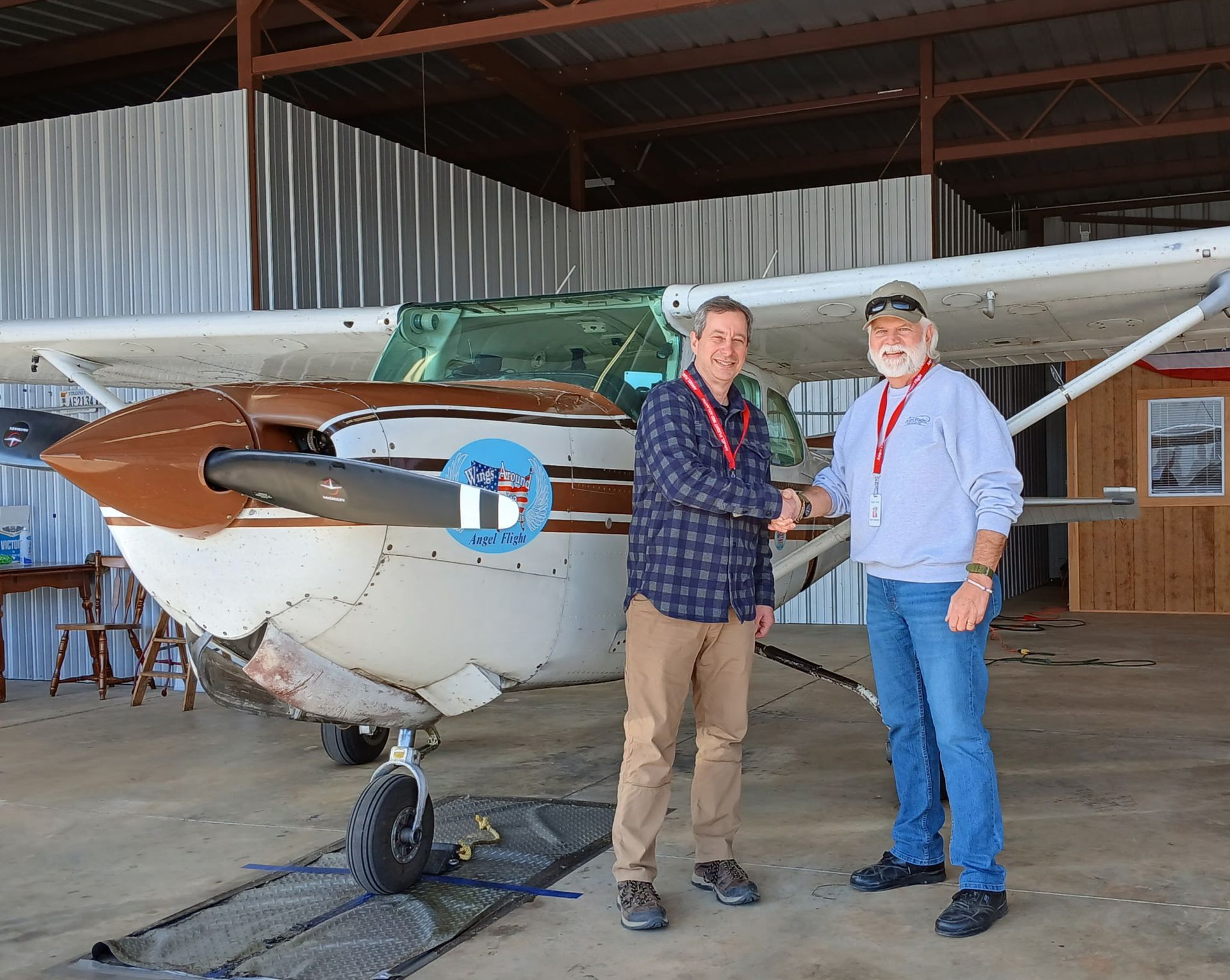 An elderly man wearing a blue hat and glasses is standing in front of a map.