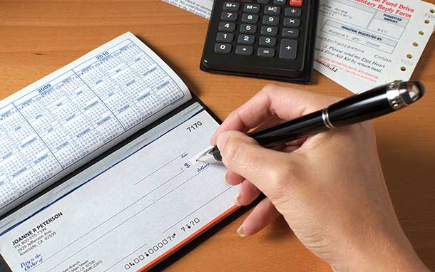A person is writing a check with a pen next to a calculator