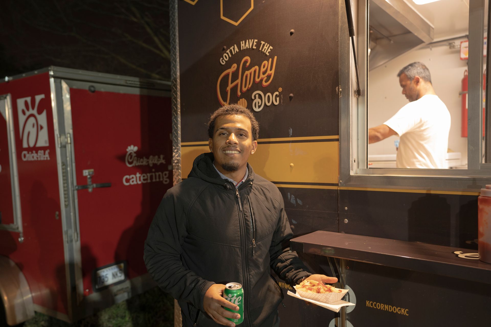 A man is standing in front of a food truck that says honey dog