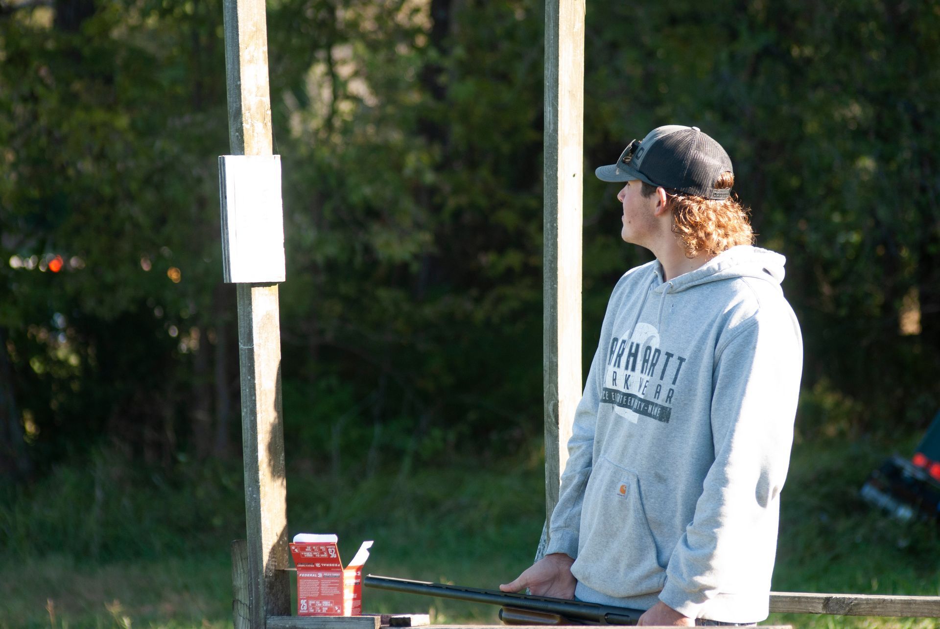 A man stand and watches as other people shoot skeet.
