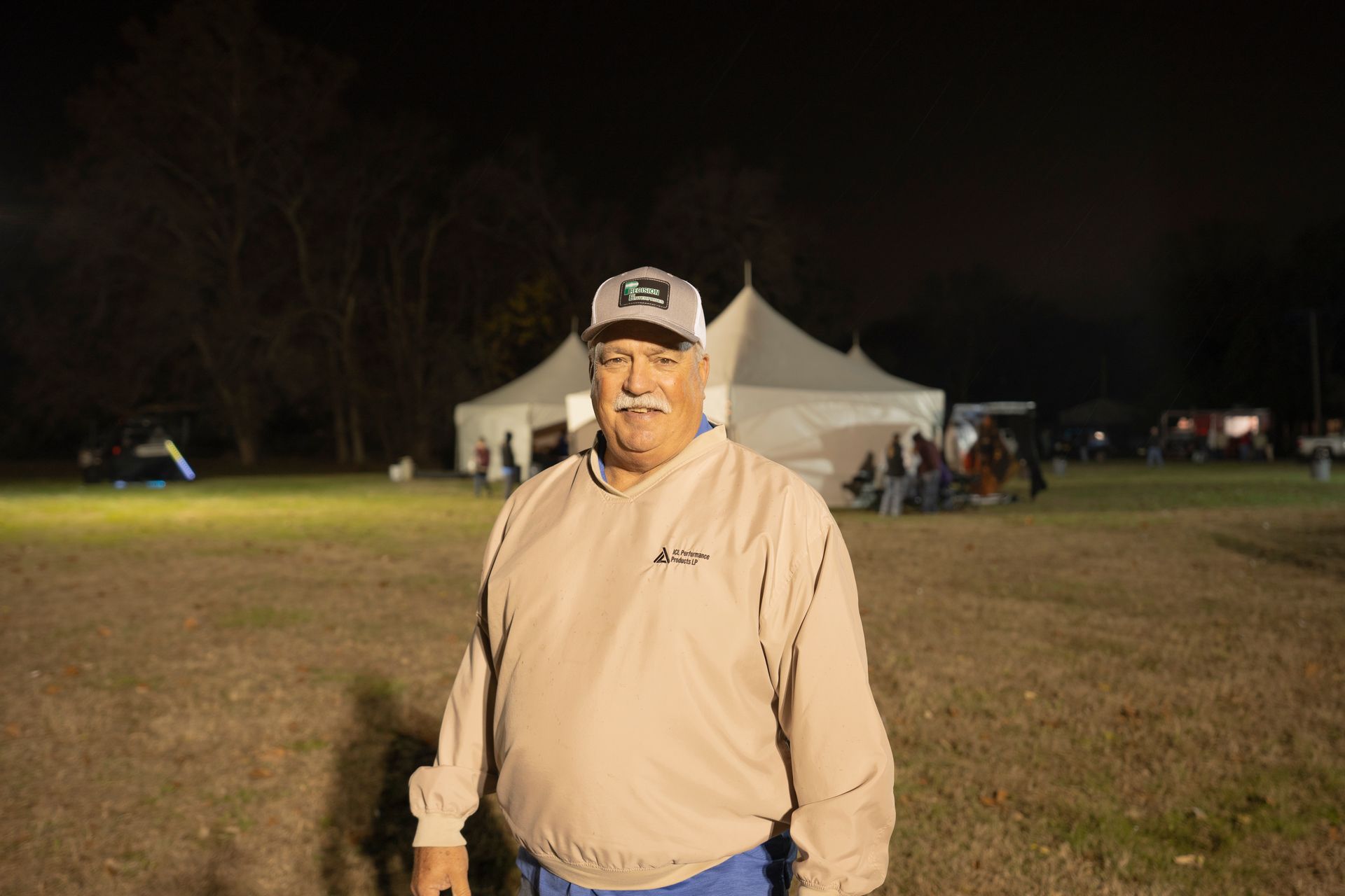 A man in a hat is standing in a field at night.