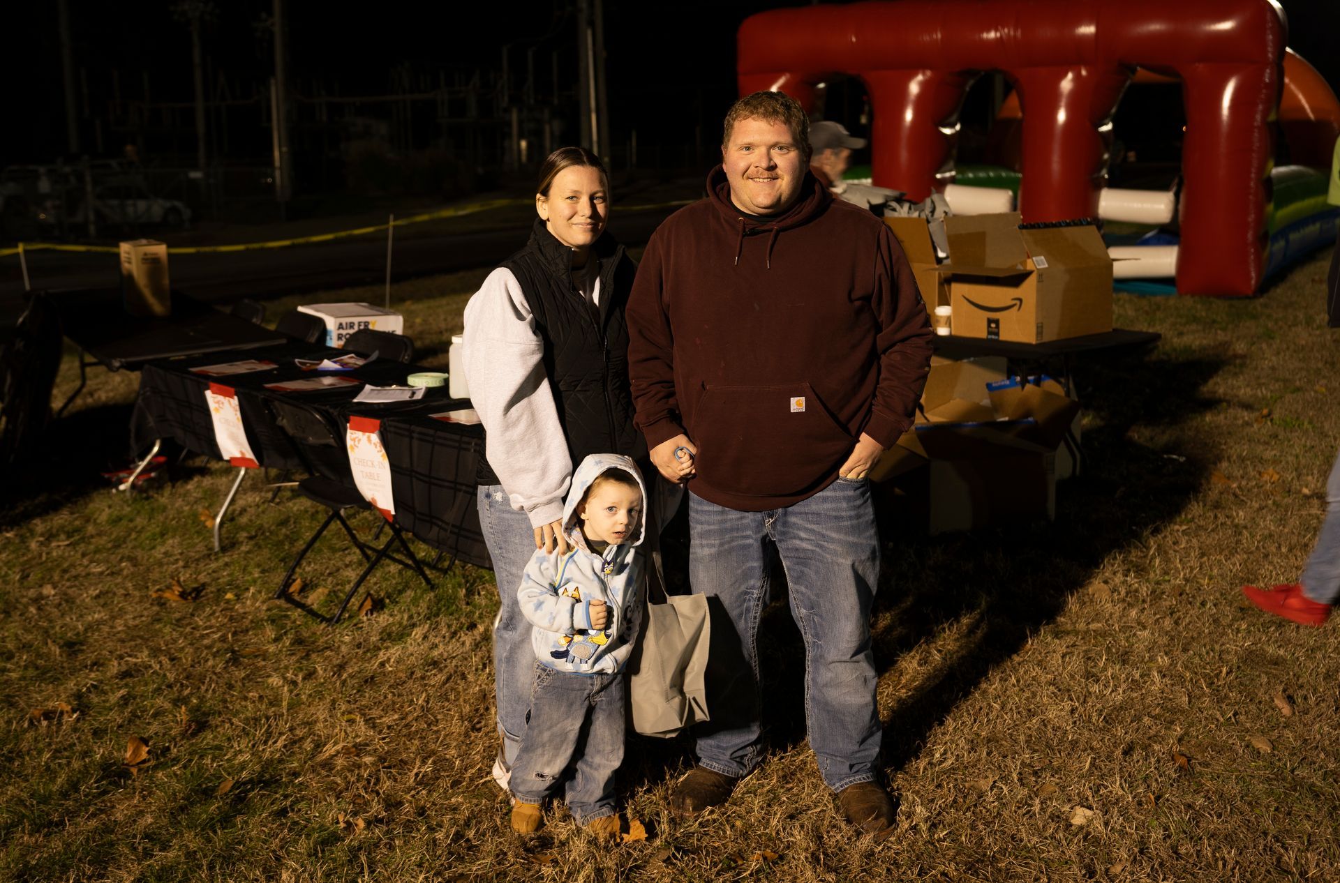 A man , woman and child are posing for a picture in front of a bouncy house.