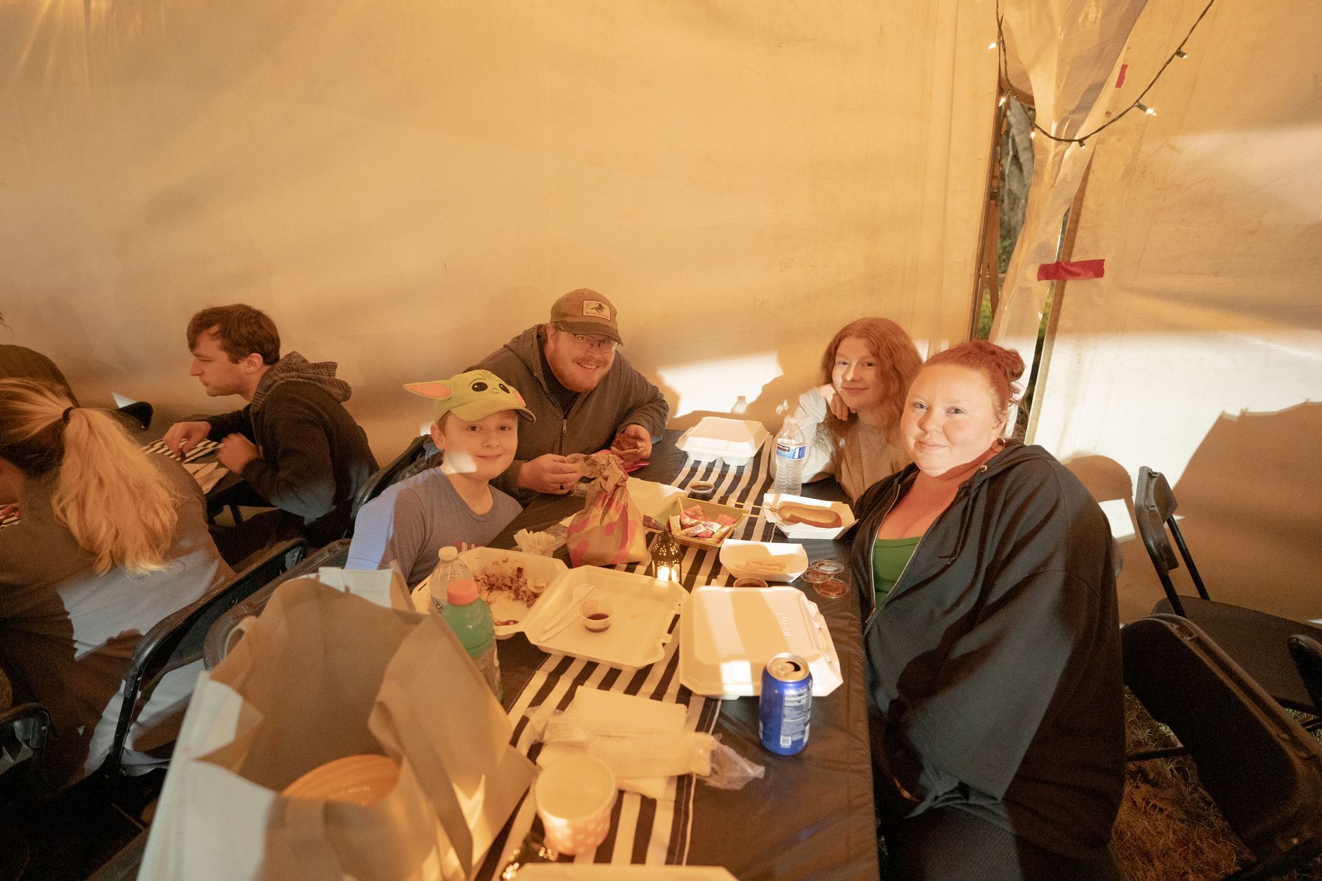 A group of people are sitting at a table in a tent eating food.