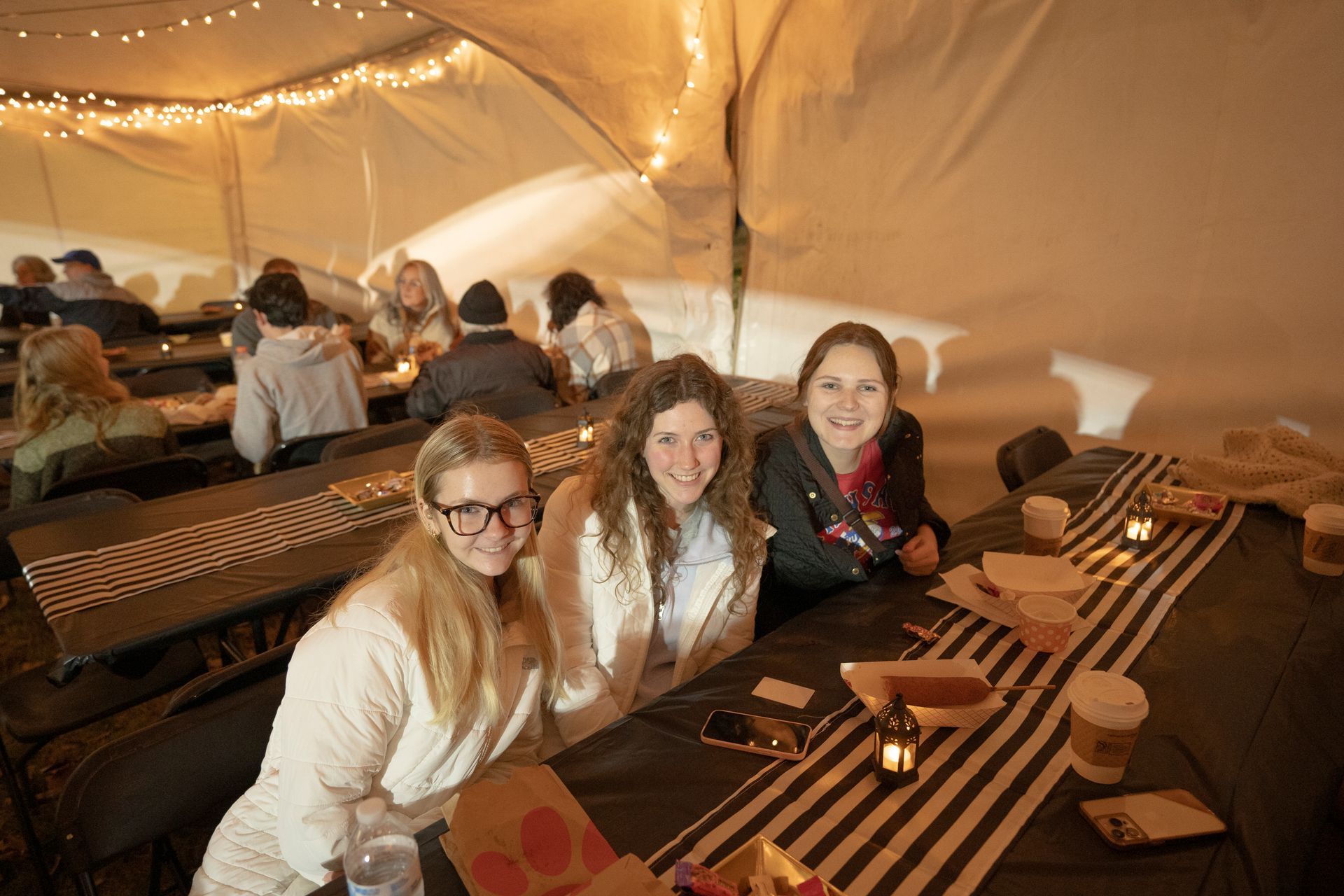 Three girls are sitting at a table in a tent.