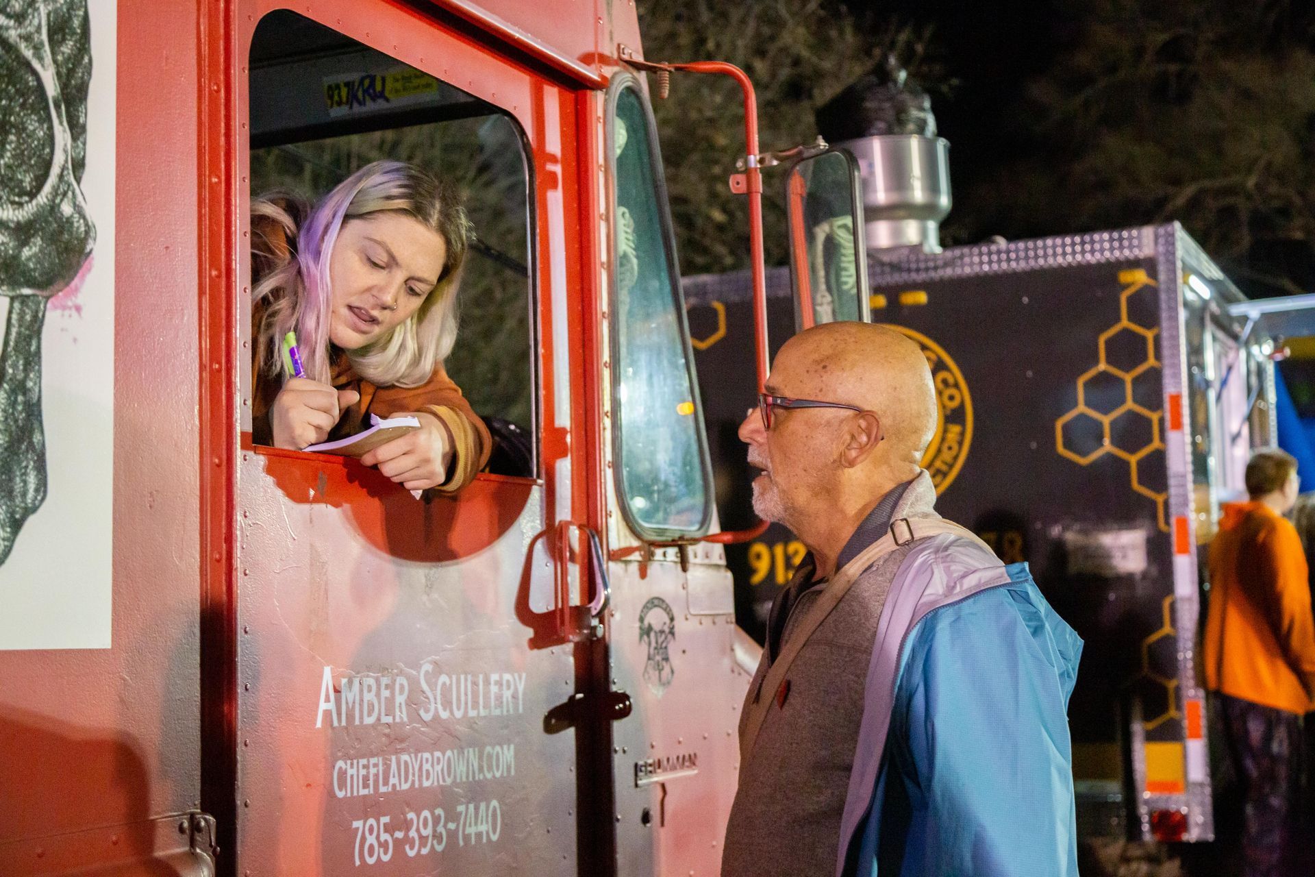 A woman in a truck is signing something for a man.