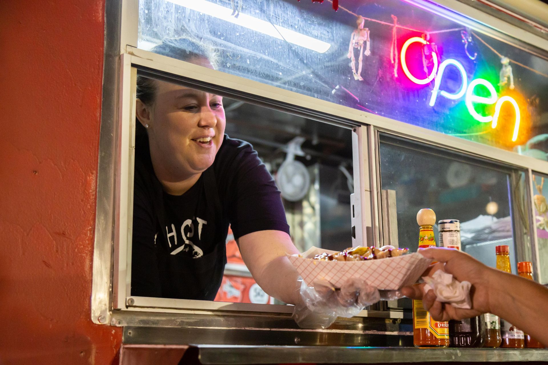 A woman hands a customer a paper bowl of food from a food truck.
