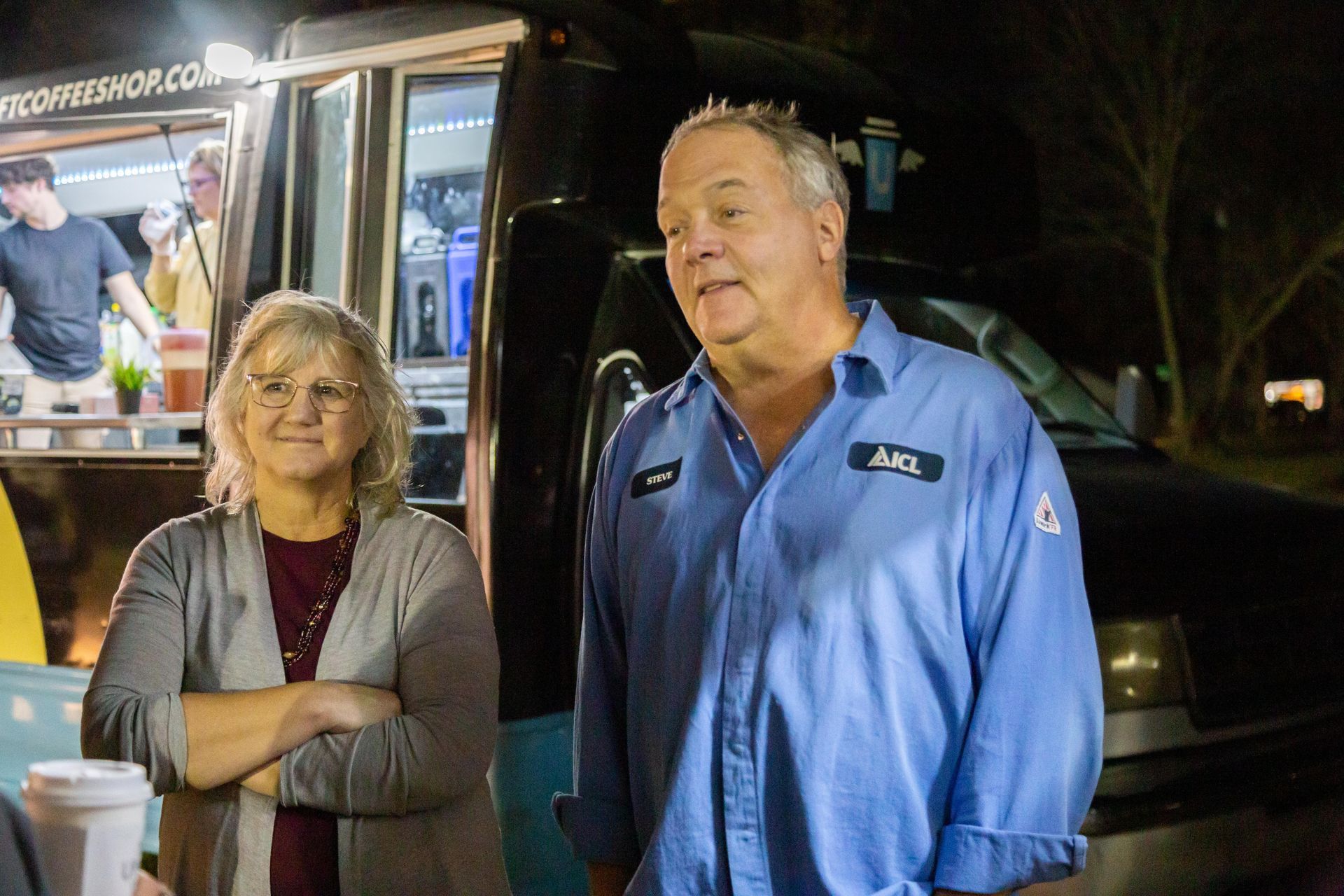 A couole stand together and smile as they are talking.