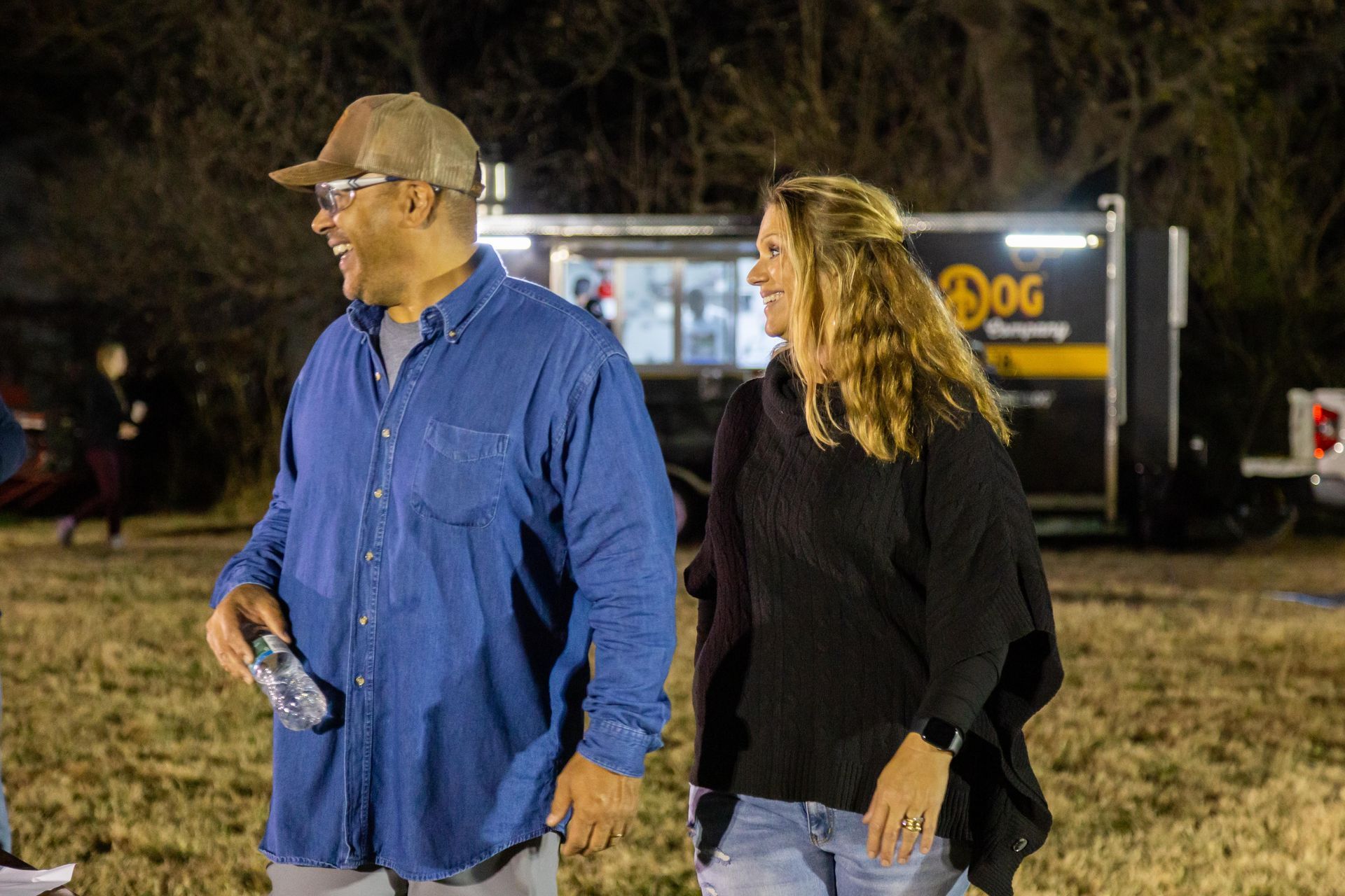A amn and woman walk togehter across the grass.