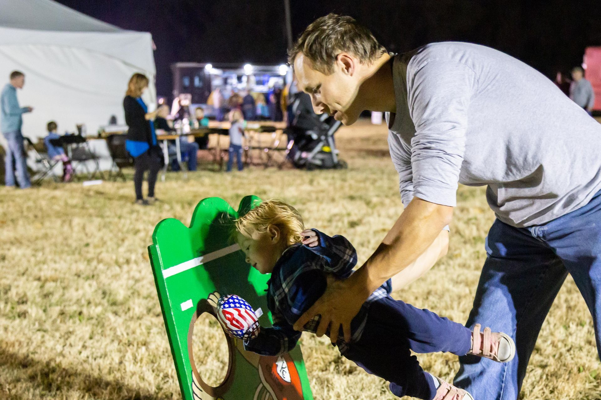 A dad helps his young son play a bean bag game.