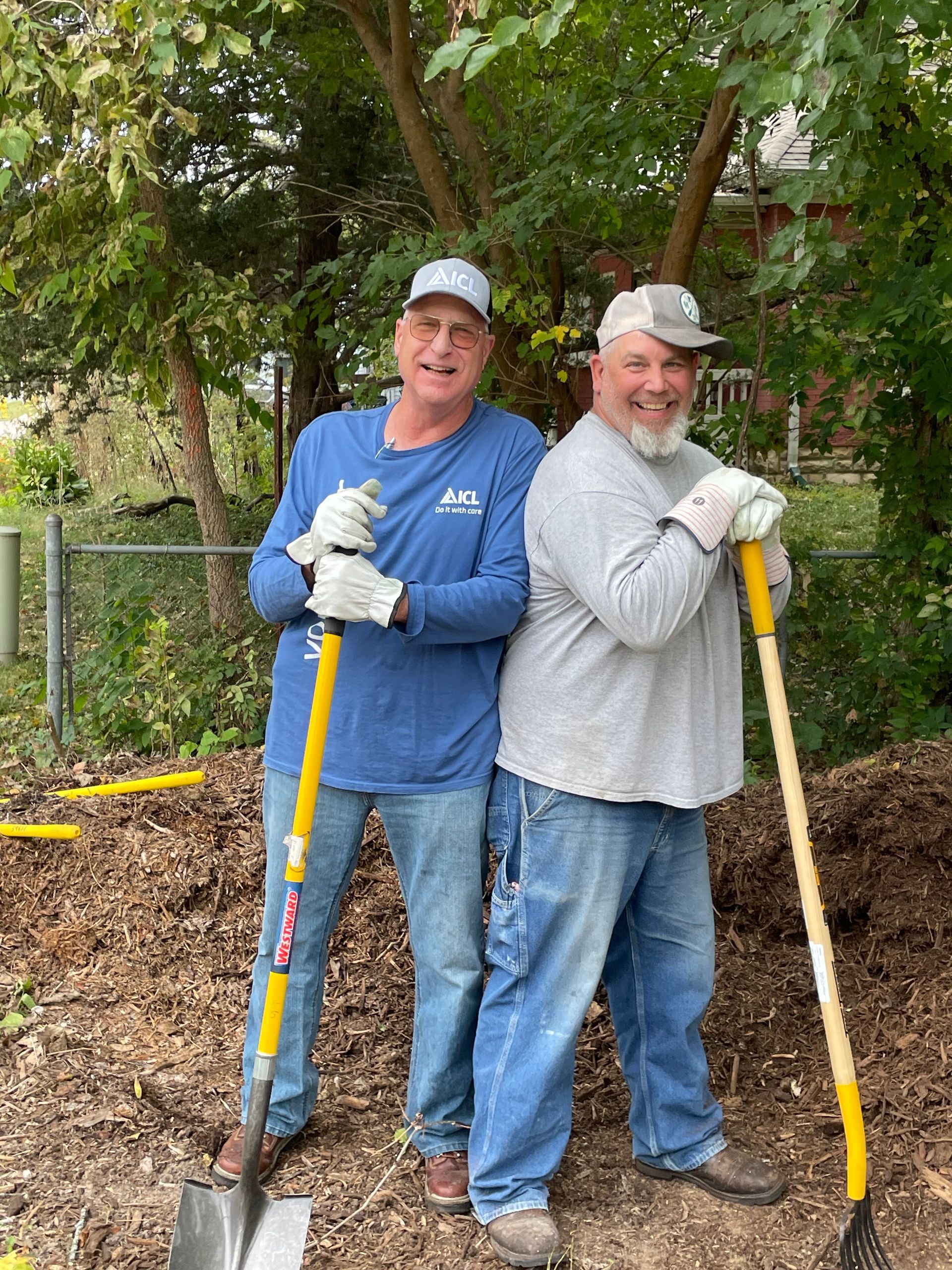 two icl employees are standing next to each other holding shovels .