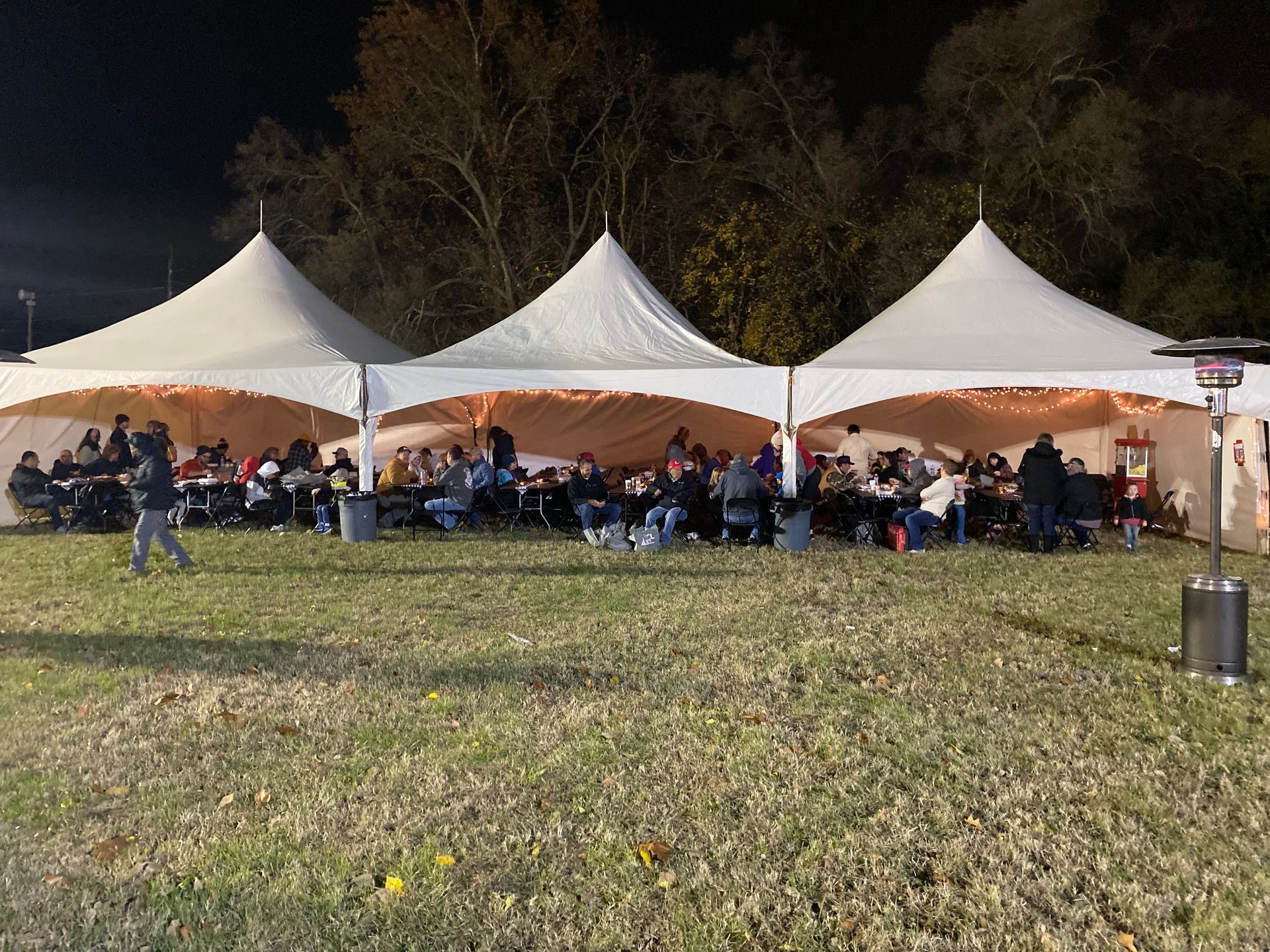 A group of people are sitting under tents in a field at night.