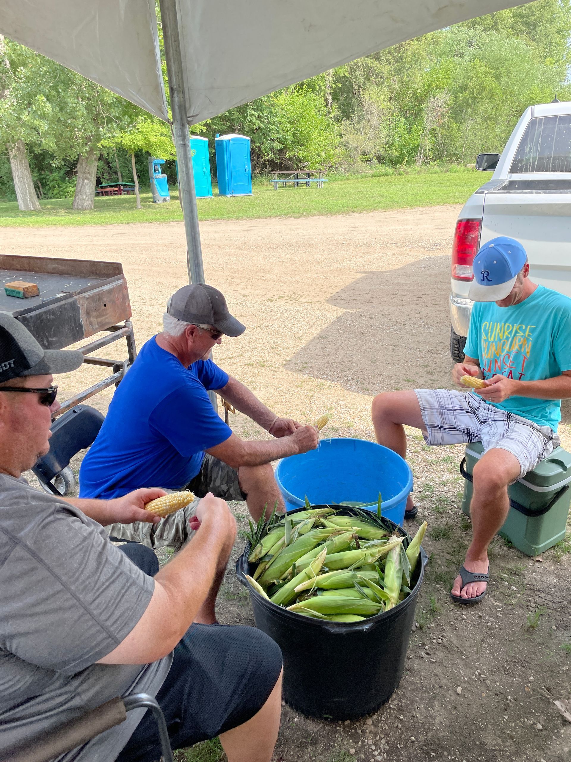 Men sit around a blue bucket to chuck corn.