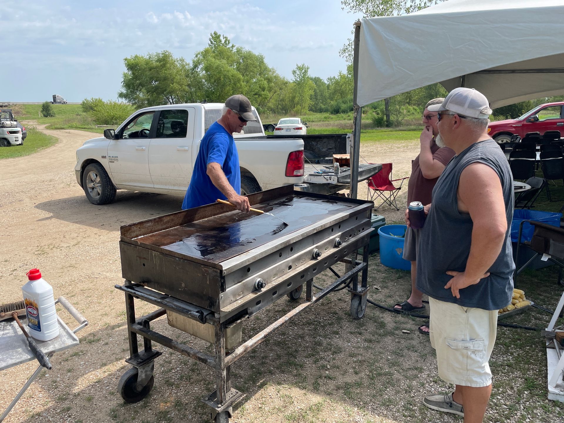 Men stand around a large grill in preparation to make burgers.