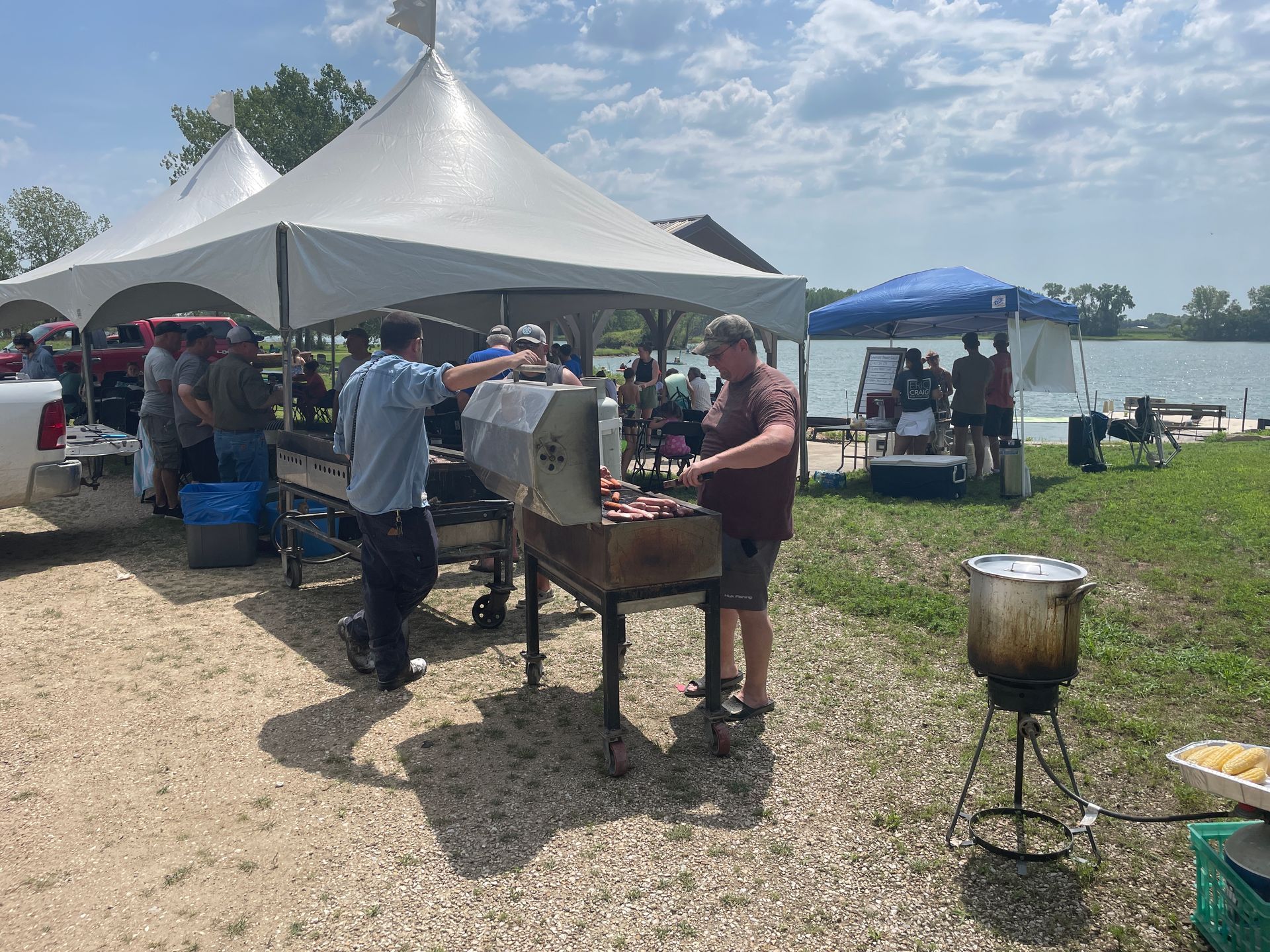 Adults are standing near a large white tent and grilling.